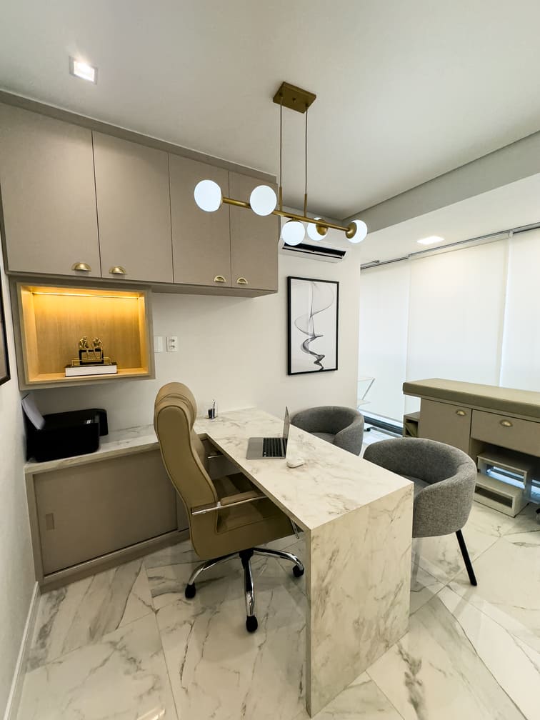Consultório médico moderno com mesa de mármore branco, cadeira executiva bege, poltronas cinza para pacientes, armários planejados e luminária pendente dourada com esferas, piso de mármore, iluminação natural suave, fotografia de interiores ultra-realista